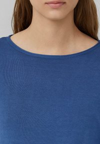 Blaues, geripptes Strickoberteil mit weitem Ausschnitt, das eine glatte Textur und eine enganliegende Form hat und hauptsächlich den Brust- und Halsbereich bedeckt.
