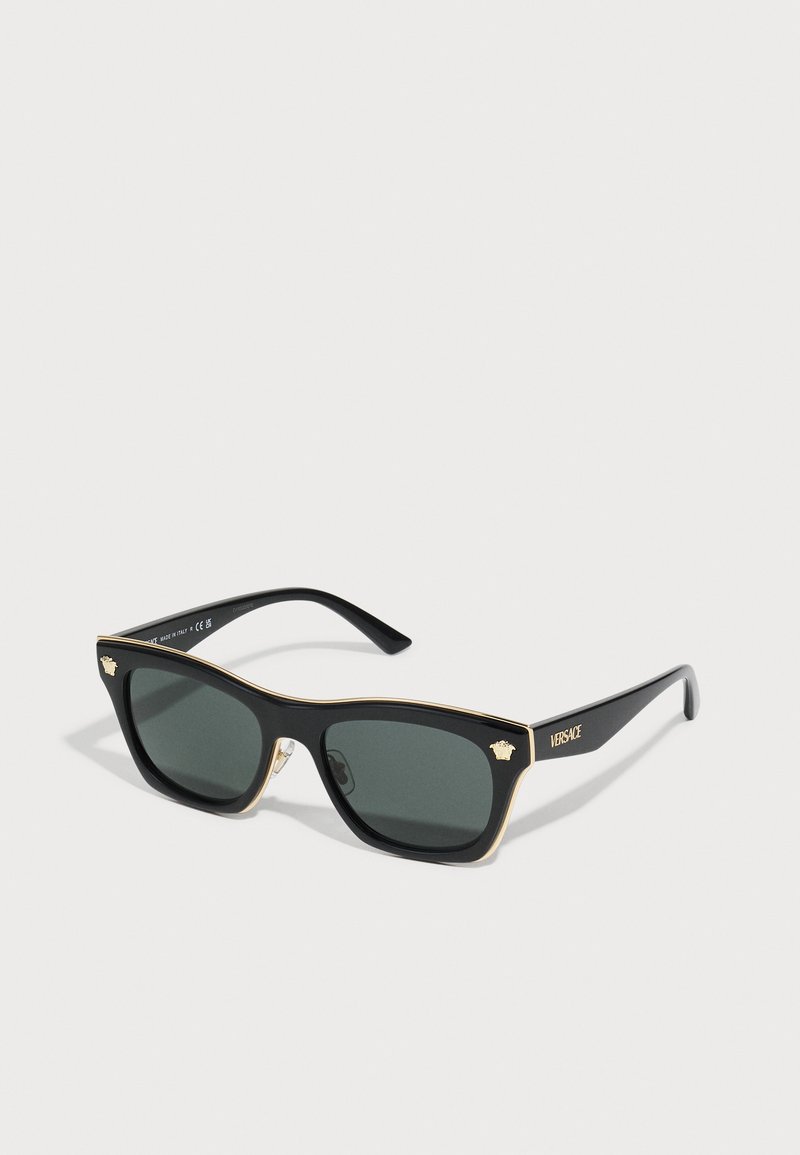 Black sunglasses with green lenses, rectangular shape, gold detailing along the top edge, and Versace logo on the side.