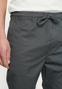 Szare spodnie dresowe z troczkiem w pasie, o gładkiej fakturze i minimalnych detalach przeszycia, prezentowane częściowo na jasnym tle.