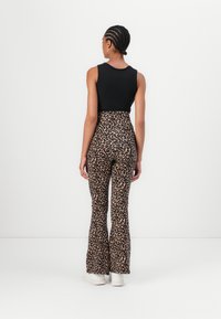 Un débardeur noir à côtes associé à un pantalon évasé à imprimé léopard à taille haute. Le modèle porte des baskets blanches et a les cheveux tressés.