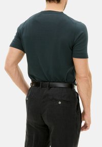 Dark green fitted t-shirt with short sleeves, paired with black linen pants featuring a back pocket and button detail, styled with a black belt.