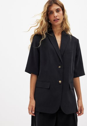 Čierny krátky rukávový blazer s klopovým golierom, dvomi prednými vreckami a zlatými gombíkmi. Hladká tkanina a voľný strih.