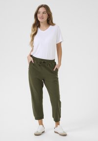 Bílý tričko s výstřihem do V, doplněné olivovými jogger kalhotami s elastickým pasem a šňůrkou, styled s bílými teniskami.