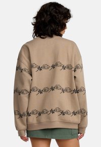 Felpa color khaki con stampa floreale nera e fiamme sulla parte posteriore e sulle maniche. Tessuto morbido, vestibilità comoda e polsini a coste.