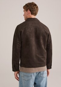 Chaqueta de ante marrón con cuello, puños abotonados y un corte casual, llevada sobre un suéter de punto beige, combinada con jeans de color azul claro.