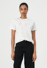 White short-sleeved T-shirt featuring pink cursive "Hugo" logo, made of cotton, paired with black pants. Smooth texture and classic fit.