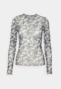 Vit långärmad genomsiktig topp med svart fjärilstryck och vågkantig röd kant vid ärmar och nederkant, visad på en enfärgad bakgrund.