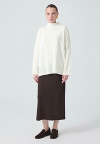 Hvid, oversized striktrøje med høj krave, parret med en mørkebrun, ankellang nederdel og brune slip-on sko.