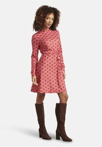 Red patterned dress with long sleeves and a wrap design, featuring a tie waist. Paired with knee-high brown suede boots.