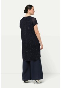 Túnica larga de punto en navy, con mangas cortas, que presenta un sutil patrón de destellos y un corte recto, combinada con pantalones de pierna ancha en navy.
