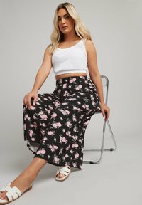 Pantaloni neri floreali con fiori rosa, cintura elastica, abbinati a un top corto bianco e sandali bianchi.