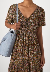 Blumenkleid mit V-Ausschnitt, kurzen Ärmeln und gerafftem Taille. Es hat kleine rosa, orange und weiße Blumen auf schwarzem Hintergrund. Helle blaue Tasche.