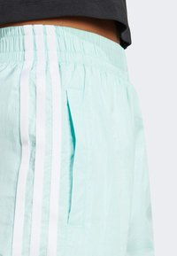 Mätové športové šortky s elastickým pásom, s tromi bielymi pruhmi po boku a bočnou kapsou so štrbinou.