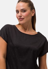 Schwarzes T-Shirt mit kurzen Ärmeln in lockerer Passform, mit einem runden Halsausschnitt und kleinen metallischen Punktschmuckelementen im gesamten Stoff.