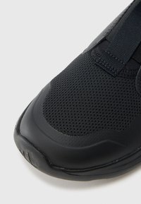 Musta urheilujalkine, jossa on verkkokangasyläosa ja sileä kumipohja. Mallissa on joustavat remmit ja pyöristetty varvasosa.