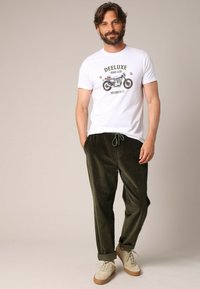 T-shirt en coton blanc avec un imprimé graphique de moto, associé à un jogging en velours côtelé vert olive, avec un cordon de serrage ajustable et des poignets retroussés.