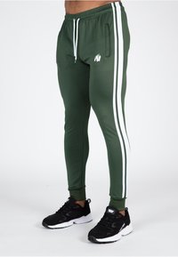 Groene sportieve joggingsbroek van gladde stof, met witte zijstreep, een elastische tailleband met trekkoord en een klein logo.
