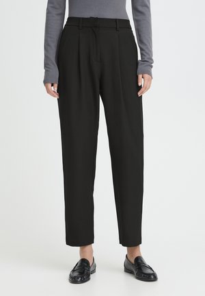 Schwarze hochtaillierte Hose mit zwei vorderen Falten, tailliertem Schnitt, zulaufendem Bein und Seitentaschen, kombiniert mit einem grauen Langarmshirt und schwarzen Loafers.