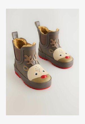 Bottes en caoutchouc marron avec un visage de renne, un nez rouge et des bois ; doublure jaune douce, semelle rouge texturée et tirant à l'arrière.