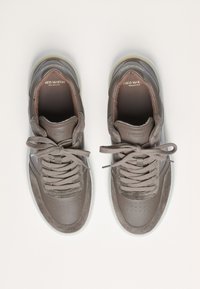 Bruine leren sneakers met een gladde afwerking, geperforeerde details, grijze suède accenten, platte veters en een doorzichtige zool.