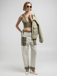 Olivgrünes geripptes Crop-Top, übergroße hellgrüne Jacke, weiße Hosen mit olivenfarbigen Flecken, kombiniert mit weißen spitzen Heels und Sonnenbrille.