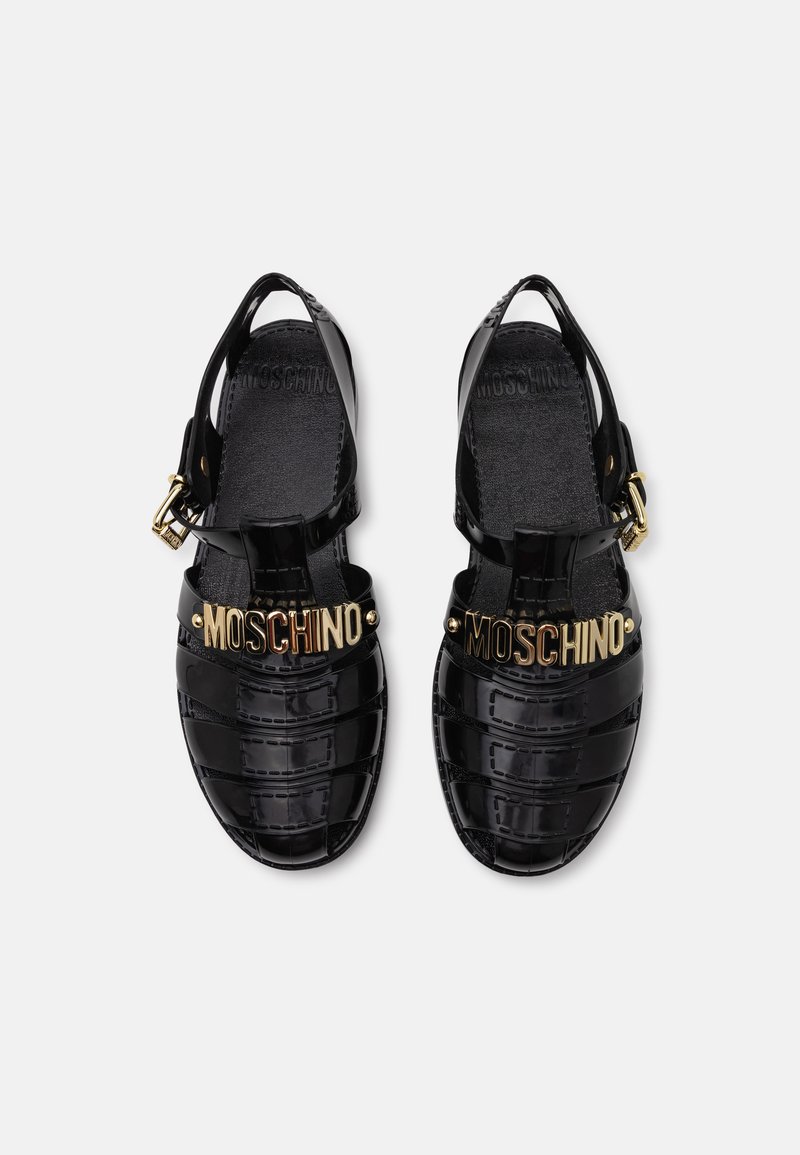 Sandales en gel noir avec design moulé, logo doré "MOSCHINO" sur les brides, boucle de cheville ajustable et semelle texturée.