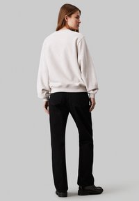 Sudadera gris clara con un corte relajado, puños acanalados y dobladillo, combinada con jeans negros de pierna recta y botas negras gruesas.