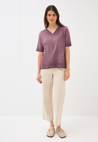Lilla kortærmet top med V-hals og lige kant, parret med cremefarvede brede bukser. Bærer beige slip-on sko.