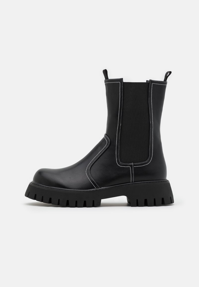 Bottines noires en cuir synthétique lisse avec des panneaux latéraux élastiques, des coutures blanches contrastantes et des semelles en caoutchouc texturé.