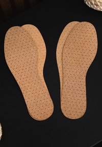 Sottili in sughero con superficie forata per la traspirabilità, forma curvata per supporto del piede e un colore beige naturale.