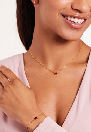 Gouden ketting en armband met een rode edelsteen als middelpunt, met een delicaat schakeldesign en een gladde textuur.
