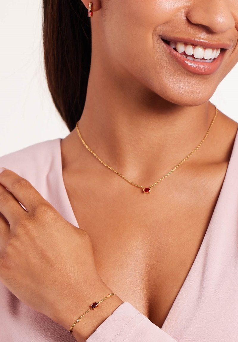 Gouden ketting en armband met een rode edelsteen als middelpunt, met een delicaat schakeldesign en een gladde textuur.