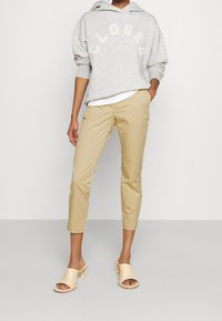 Grå hoodie med "CLOSED" tryckt i vitt, beige beskurna byxor och ljus beige öppna tofflor med blockklack. Mjuka texturer, avslappnad passform.