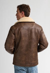 Chaqueta de cuero marrón con un cuello de borrego, que presenta una textura suave, un peso medio y un diseño estructurado. La vista trasera muestra costuras simples.