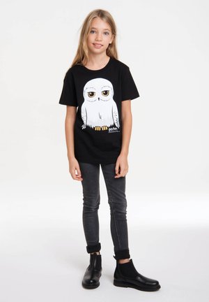 Black t-shirt featuring a cartoon white owl design. The child wears dark skinny jeans and black ankle boots with elastic sides.