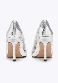 Scarpe di alta moda metalliche argento con punta appuntita, superficie texturizzata e stiletto sottile. Presentano delicate cuciture e branding.