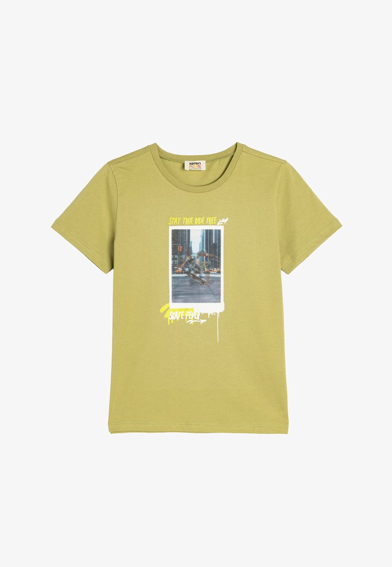 Camiseta de manga corta de color verde oliva hecha de algodón. Presenta un estampado gráfico con texto y una foto de un patinador en la parte frontal.