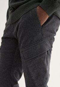 Donkergrijze cargobroek met een gestructureerde stof, zijzak en zichtbare stiksels, ontworpen voor comfort en functionaliteit.