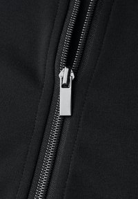 Primo piano di tessuto nero con cerniera, che mostra una cerniera metallica con una linguetta rettangolare e una superficie strutturata attorno all'area della cerniera.