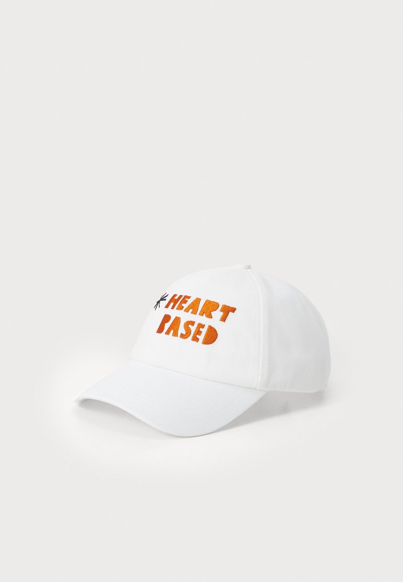 Balta beisbolo kepurė su oranžiniu siuvinėtų tekstu „HEART BASED“ priekyje, struktūruota karūna ir lenktu kraštu.