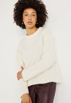 Cremfarbener Strickpullover mit Rundhalsausschnitt, gerippten Bündchen und lockerer Passform. Kombiniert mit bordeauxroten, hochtaillierten Hosen. Weicher Komfort.