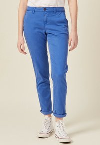 Blauwe katoenen chinos met een slim fit, opgerolde mouwen en een knoopsluiting. Draagt bij witte hoge sneakers. Glad textuur en casual ontwerp.