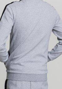 Grå sweatshirt med rund hals, långa ärmar och ribbade avslut. Har svarta sidodetaljer och en slät, strukturerad tyg.