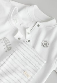 Weißes Babyoutfit mit geripptem Kragen, Druckknöpfen und dem Schriftzug "HELLO WORLD". Inklusive einer grauen gestreiften Tasche mit "happy"-Etikett.