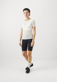 Kurzarmpullover aus transparentem Weiß, kombiniert mit eng anliegenden schwarzen Radshorts. Verfügt über einen runden Ausschnitt und kontrastierende Texturen. Schwarze Radschuhe und weiße Socken.