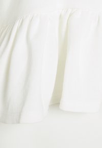 Tessuto di cotone bianco con un ruffle arricciato all'orlo. Texture liscia, leggero e presenta cuciture ordinate lungo i bordi.