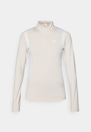Ljusbeige långärmad topp med halvdragkedja i kragen. Har vita sidopaneler och en liten logotyp på bröstet. Slät, elastisk tyg.