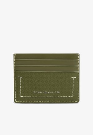 Smukły oliwkowozielony skórzany etui na karty z teksturowaną przednią stroną, białym przeszyciem i logiem Tommy Hilfiger na dole na środku.