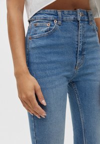High-waisted blue denim jeans with copper rivets, five-pocket design, and subtle fading. Smooth texture with a straight-leg cut.