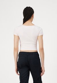 Világos rózsaszín, testhezálló, rövid ujjú crop top. Simaság jellemzi és kör alakú nyakú. Fekete, rugalmas derekú cargo nadrággal viselve.